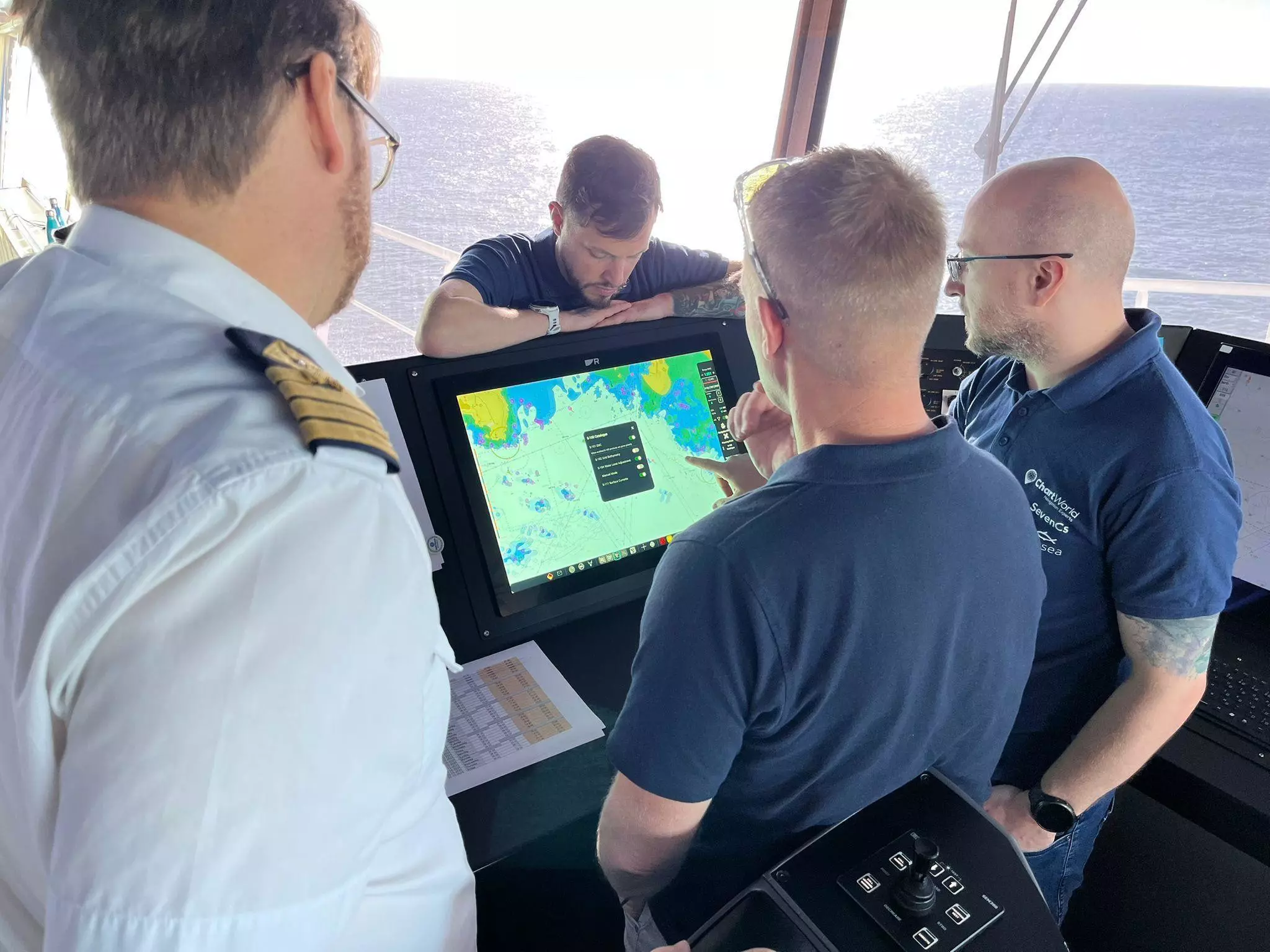 Group of men, including Andy Murray from ChartWorld, looking at electronic chart display which includes S-100 and ECDIS.